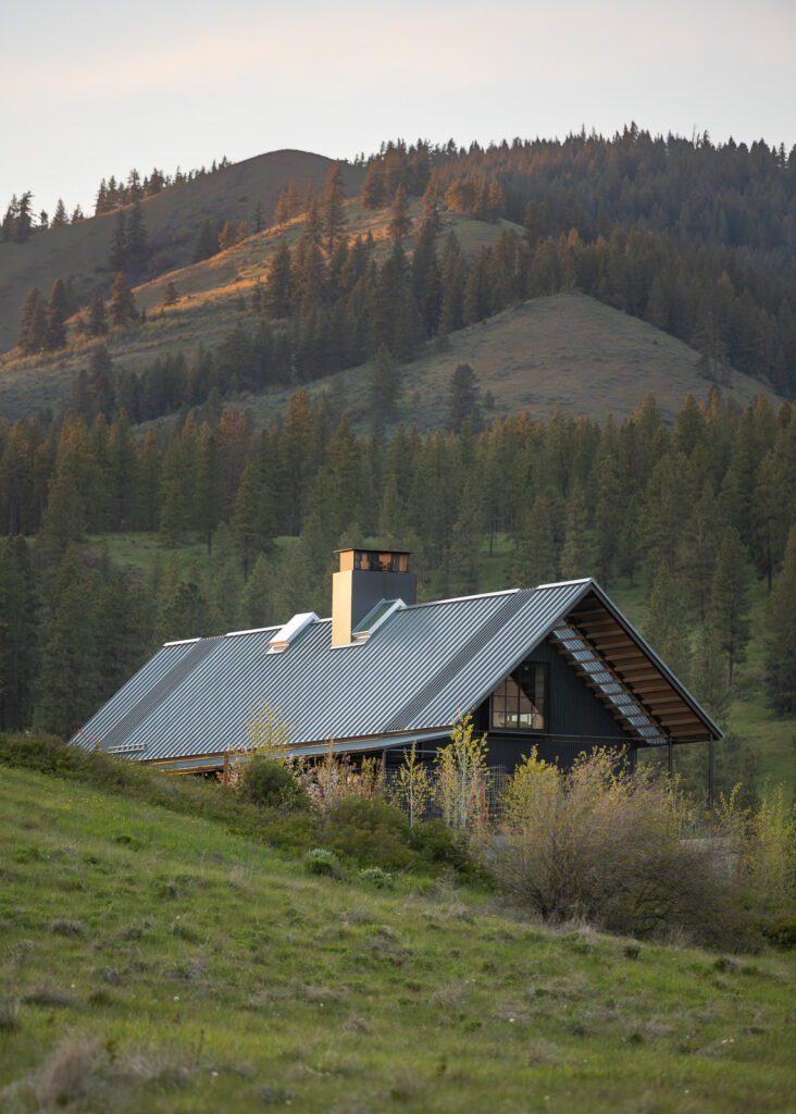 An exterior view of a dwelling with gabled black raised rib metal roof mimicking the surrounding mountains.